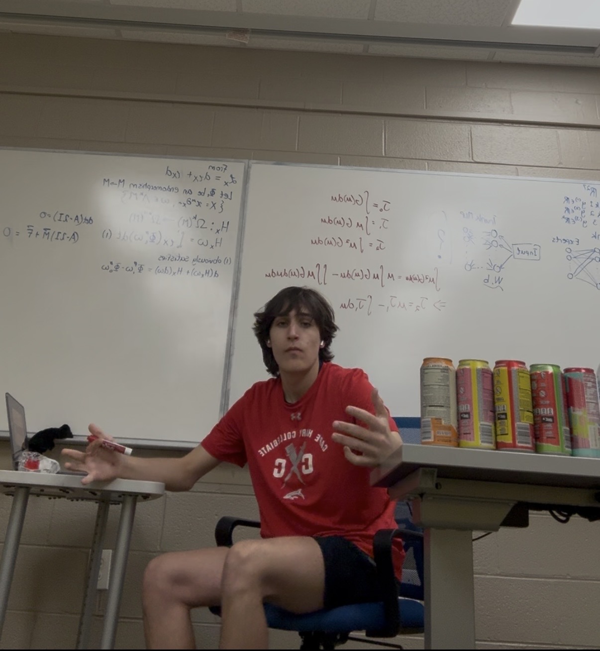 John sitting in front of a whiteboard covered with equations
